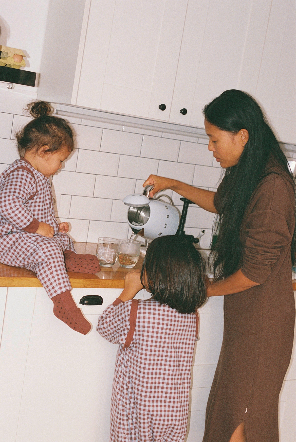 Madre con sus dos hijos preparando infusión en la cocina de casa durante una sesión de fotos para la marca de pijamas Molis&Co
