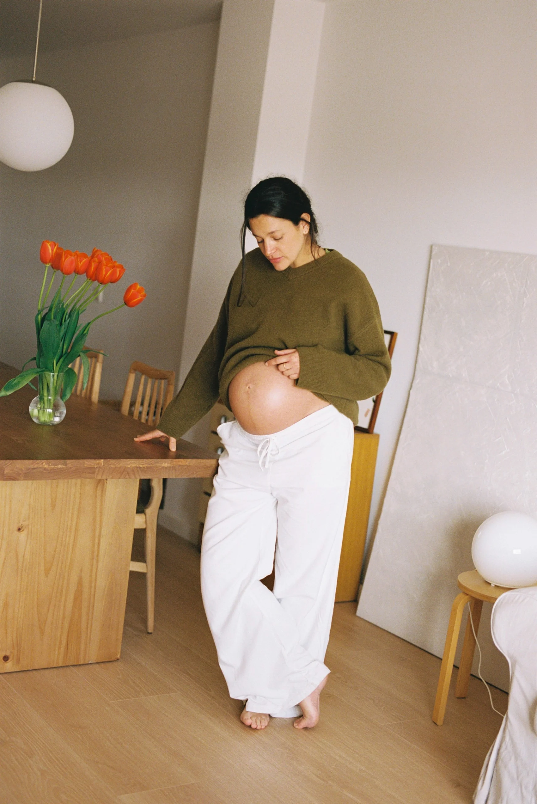 Mujer embarazada contempla su barriga durante una sesión de maternidad hecha con luz natural y en formato analógico en su casa de Sabadell