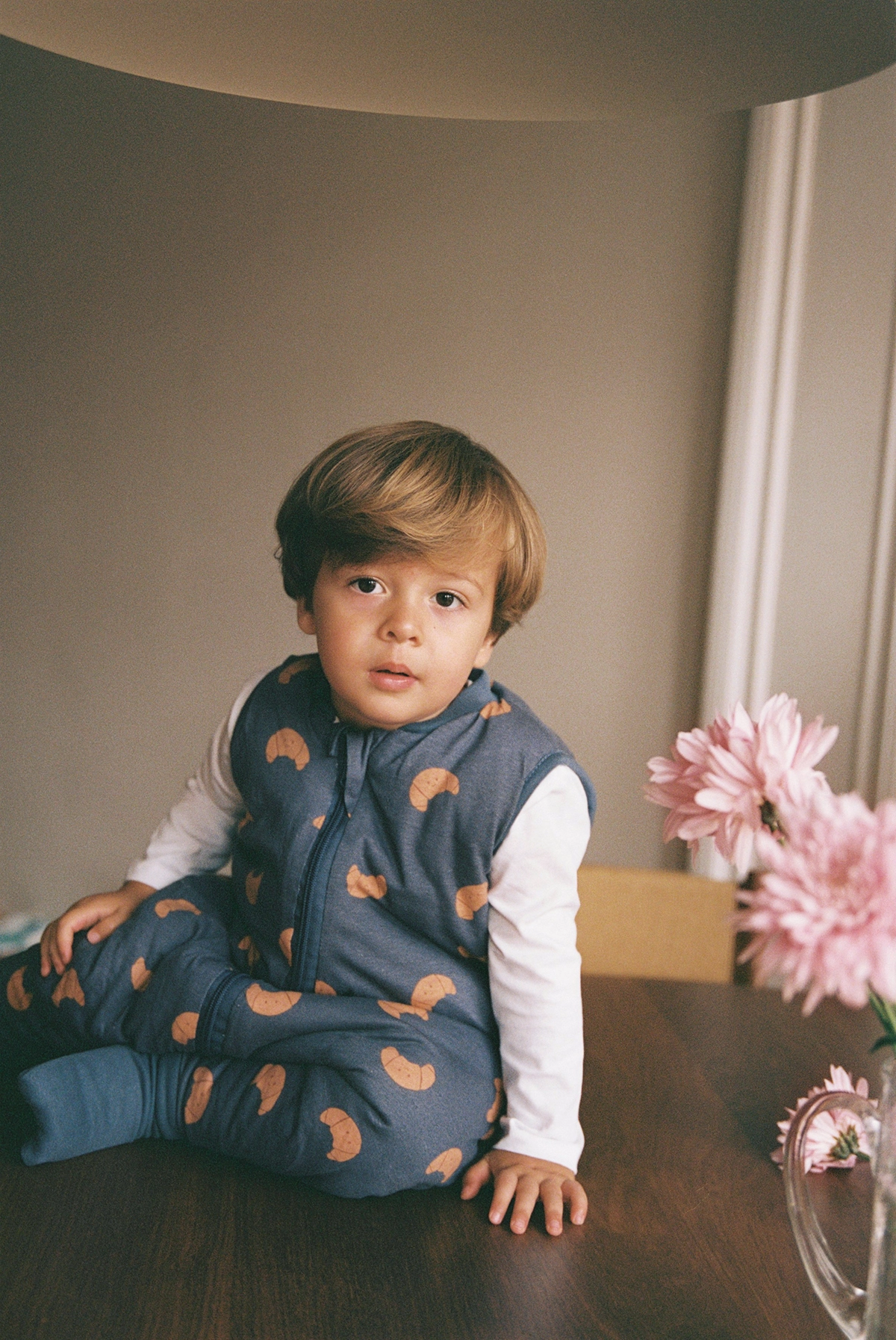 Niño con pijama de Molis&Co sentado en una mesa junto a flores